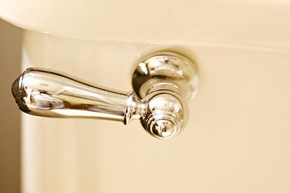 De loodgietersplamuur van de bodem van het toilet met een plamuurmes